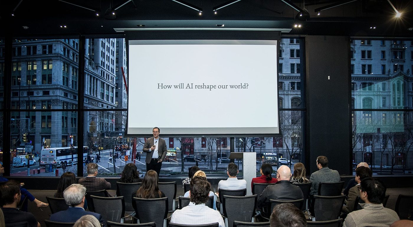 Dror Poleg on stage in front of a screen reading “How will AI reshape our world?”